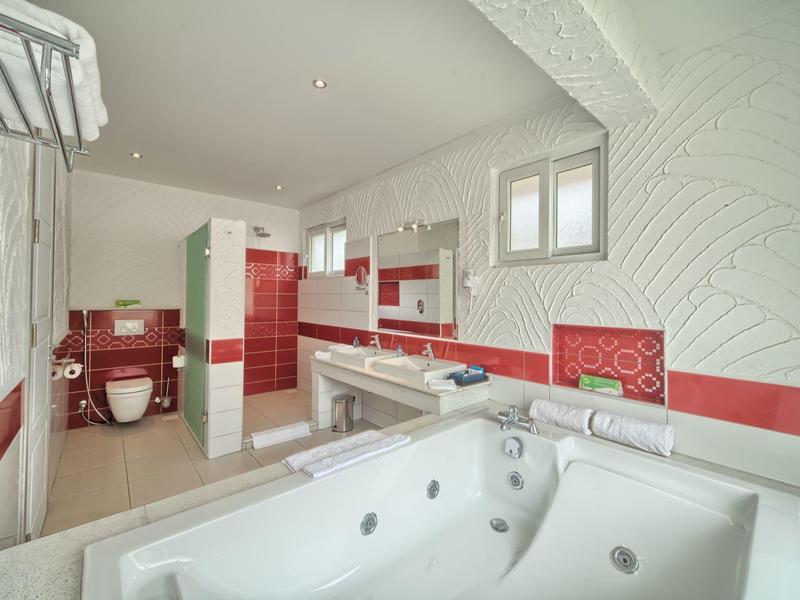 Světlá koupelna s červeným obkladem, vířivkou a samostatnou toaletou.