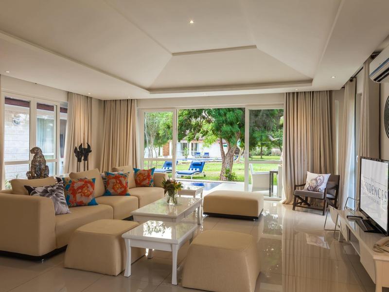 Světý obývací pokoj s pohovkami, konferenčním stolkem a výhledem na zahradu s bazénem.