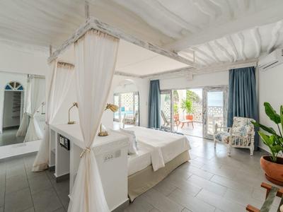 Chambre d'hôtel élégante avec lit à baldaquin, coin salon et accès à la terrasse avec vue sur la verdure.