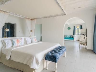 Chambre lumineuse avec grand lit, rideaux bleus et arche menant au salon.