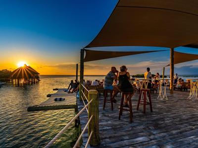 Coucher de soleil sur un lac avec une terrasse où les gens s'assoient et profitent de boissons.