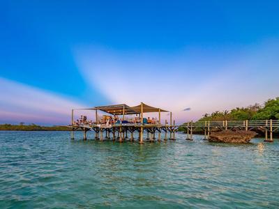 Un restaurant sur pilotis au-dessus d'une eau bleu clair avec un ciel nuageux en arrière-plan.