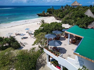 Complexe balnéaire avec sable blanc, palmiers et un bâtiment au toit vert au bord de la mer