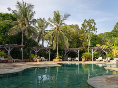 Schwimmbad mit Palmen und Pavillons vor grüner Vegetation an einem klaren Tag.