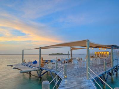 Offenes Restaurant auf einem Steg über ruhigem Wasser bei Sonnenuntergang.