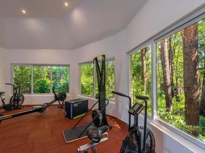 Helles Fitnesszimmer mit großen Fenstern und Blick auf Bäume im Grünen.