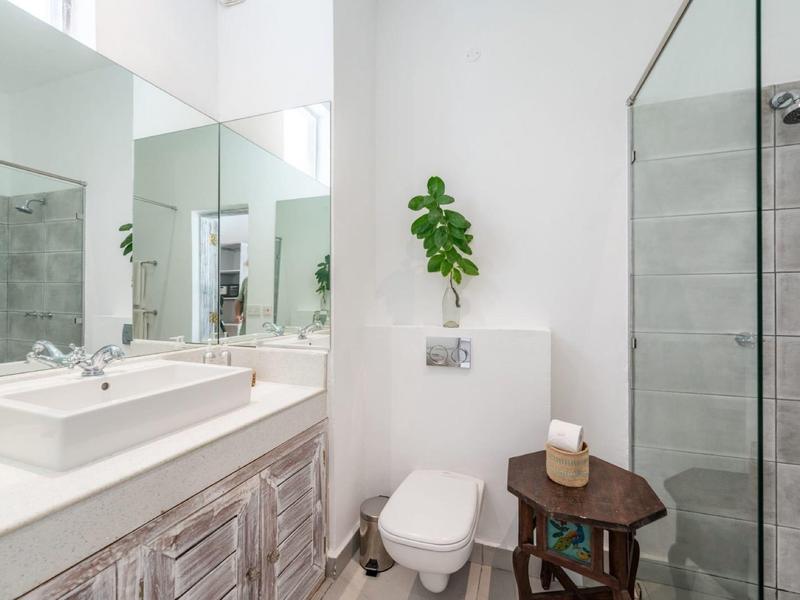 Salle de bain moderne avec murs blancs, lavabo, toilettes et douche avec porte en verre.