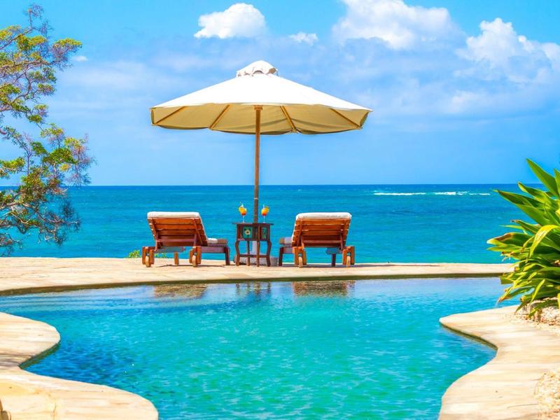 Deux chaises longues et un parasol à côté d'une piscine avec vue sur la mer bleue.