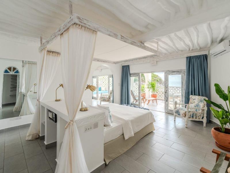 Chambre d'hôtel élégante avec lit à baldaquin, coin salon et accès à la terrasse avec vue sur la verdure.