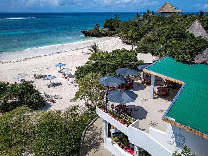 Complexe balnéaire avec sable blanc, palmiers et un bâtiment au toit vert au bord de la mer