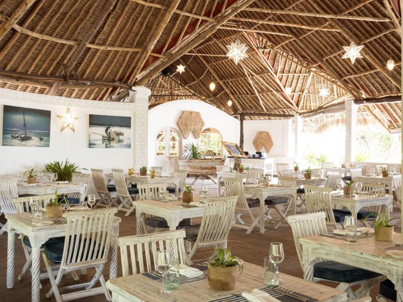 Restaurant lumineux et ouvert avec toit en chaume et tables dressées.