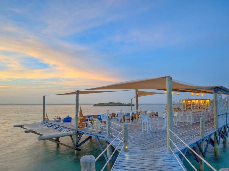 Restaurant de plage avec mobilier bleu et blanc sur une jetée au coucher du soleil