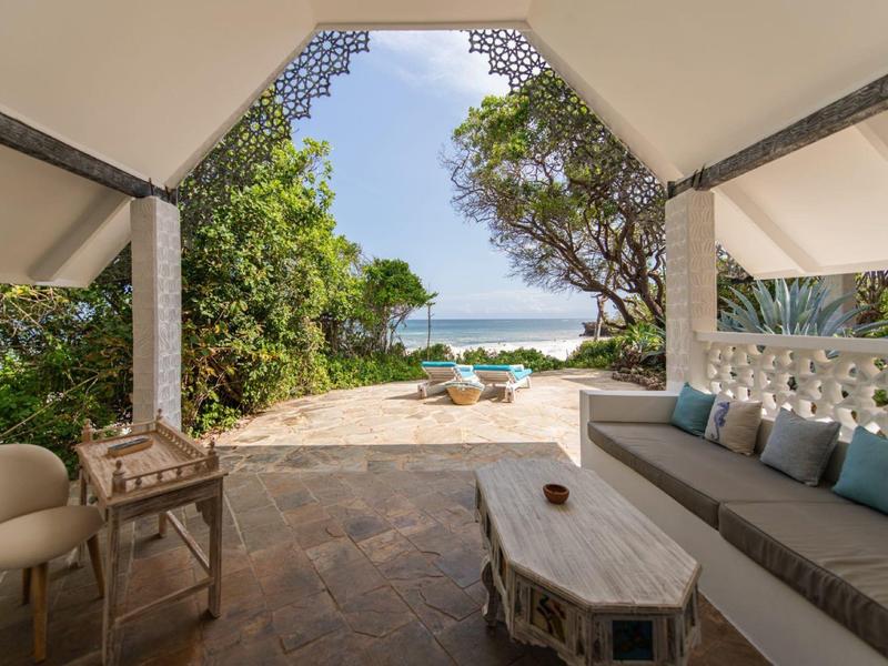 Terrasse couverte avec coin salon donnant sur des chaises de plage et vue sur l'océan.