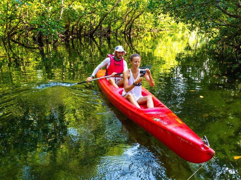 Deux personnes pagayant dans un kayak rouge sur une rivière calme entourée d’arbres.