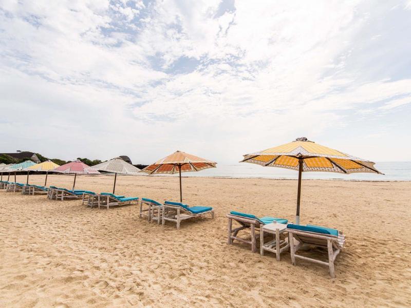 Chaises longues vides avec parasols sur la plage de sable sous un ciel nuageux.