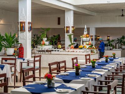 Ampia sala da pranzo con lunghi tavoli, stoviglie blu e decorazioni floreali.