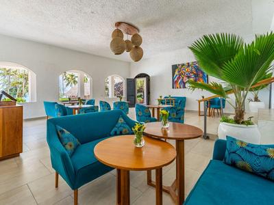 Lounge dell'hotel luminoso con divani blu, tavoli in legno e grandi piante.