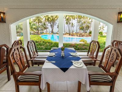 Zona pranzo con tavolo apparecchiato e vista sulla piscina e palme esterne.
