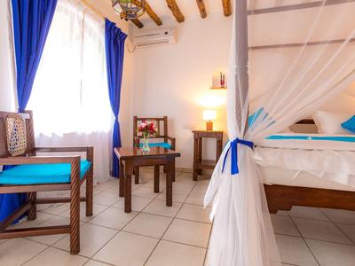 Camera d'albergo luminosa con mobili in legno, dettagli blu e letto con zanzariera.