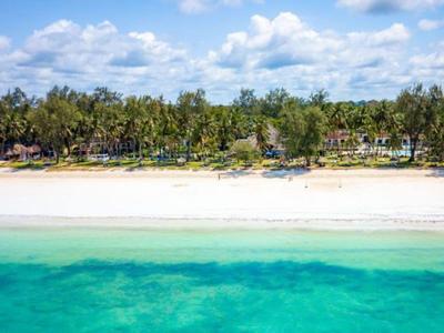 Spiaggia di sabbia bianca con acqua turchese e costa boscosa sotto cielo soleggiato.