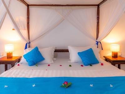 Letto matrimoniale con zanzariera, cuscini blu e comodini con lampade in una camera d'hotel.