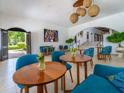 Accogliente zona lounge dell'hotel con poltrone blu, tavoli in legno e piante decorative.