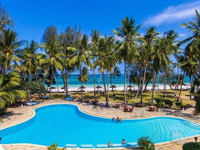 Palmen umrahmen großen, geschwungenen Pool mit Blick auf Sandstrand und blaues Meer unter klarem Himmel.