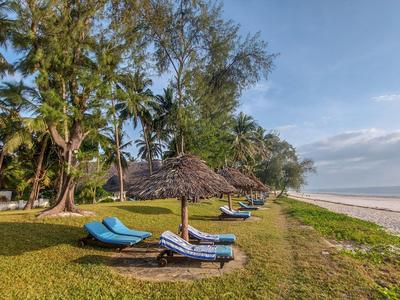 Strand mit Liegestühlen und Sonnenschirmen auf einer Wiese neben dem Sandstrand und Palmen.