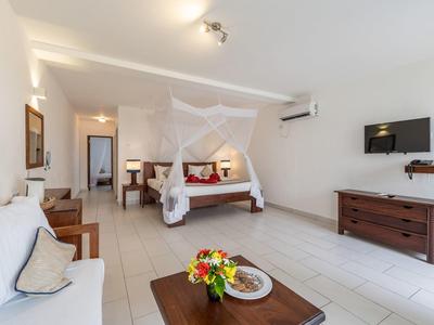 Camera d'hotel luminosa con letto a baldacchino, divano, fiori sul tavolo e TV a parete.