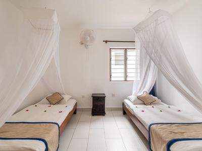 Camera d'hotel luminosa con due letti singoli e zanzariere accanto a una finestra.