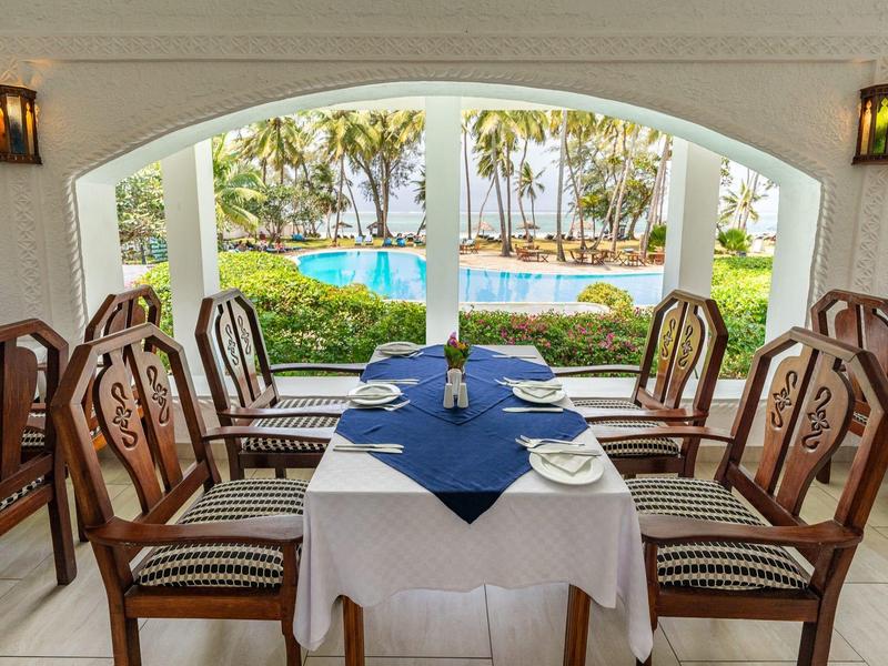 Zona pranzo con tavolo apparecchiato e vista sulla piscina e palme esterne.
