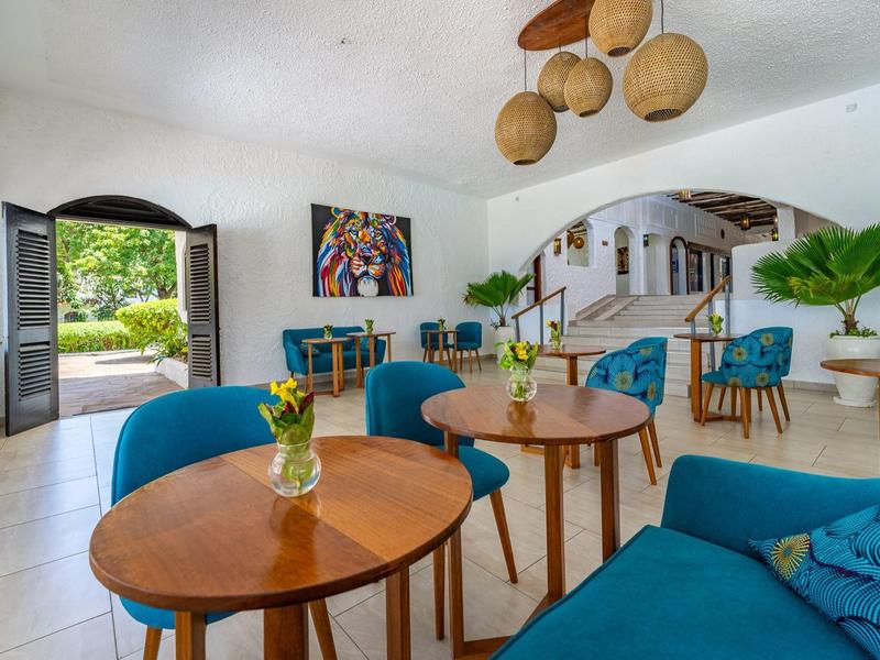 Accogliente zona lounge dell'hotel con poltrone blu, tavoli in legno e piante decorative.