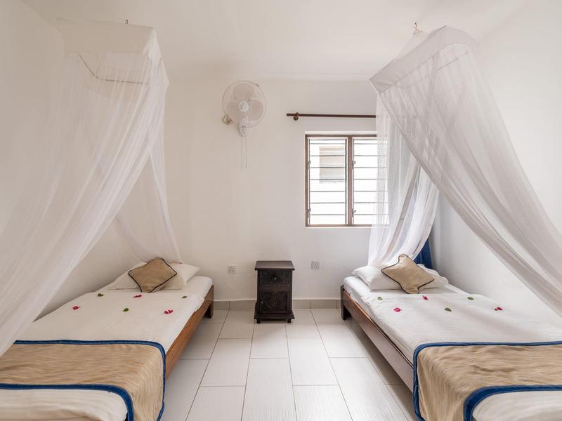 Camera d'hotel luminosa con due letti singoli e zanzariere accanto a una finestra.