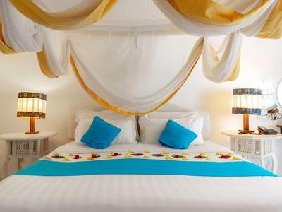 Lichte hotelkamer met comfortabel tweepersoonsbed, witte en blauwe accenten en decoratieve stoffen aan het plafond.