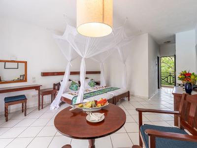 Lichte hotelkamer met hemelbed, klamboe en balkon met uitzicht op groen.