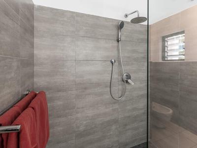 Moderne badkamer met inloopdouche, grijze tegels en rode handdoeken.