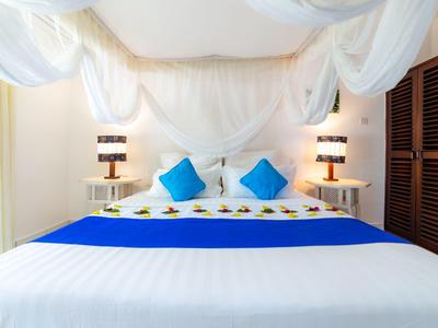 Lichte slaapkamer met groot bed, blauwe kussens en witte gordijnen aan het plafond.