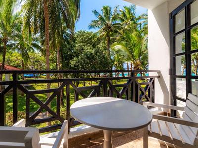 Balkon met ronde tafel en stoelen met uitzicht op tropische palmbomen en blauwe lucht.