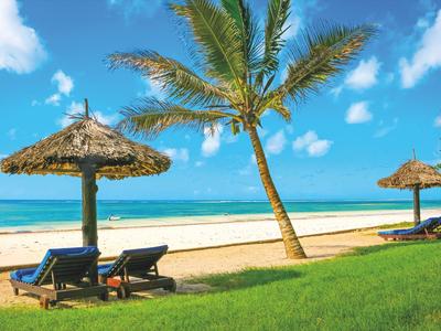 Strand mit Palmen, Liegestühlen und Strohdächern unter blauem Himmel.