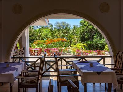 Uitzicht vanuit een schaduwrijk restaurant met gedekte tafels op een zonnige, bloeiende tuin.