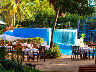 Außenterrasse eines Hotels mit gedeckten Tischen und Blick auf einen Pool mit Wasserfall.