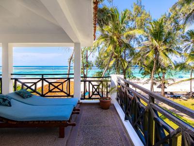 Balkon met ligstoel met uitzicht op strand en palmbomen onder blauwe lucht.