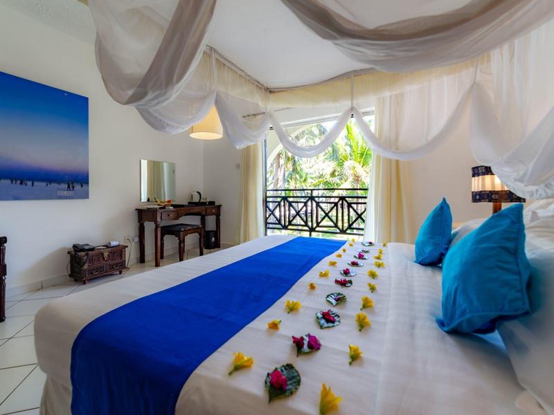 Lichte hotelkamer met groot bed, blauwe kussens en uitzicht op balkon.