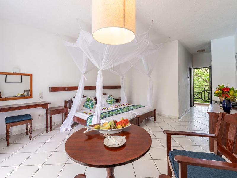 Lichte hotelkamer met hemelbed, klamboe en balkon met uitzicht op groen.