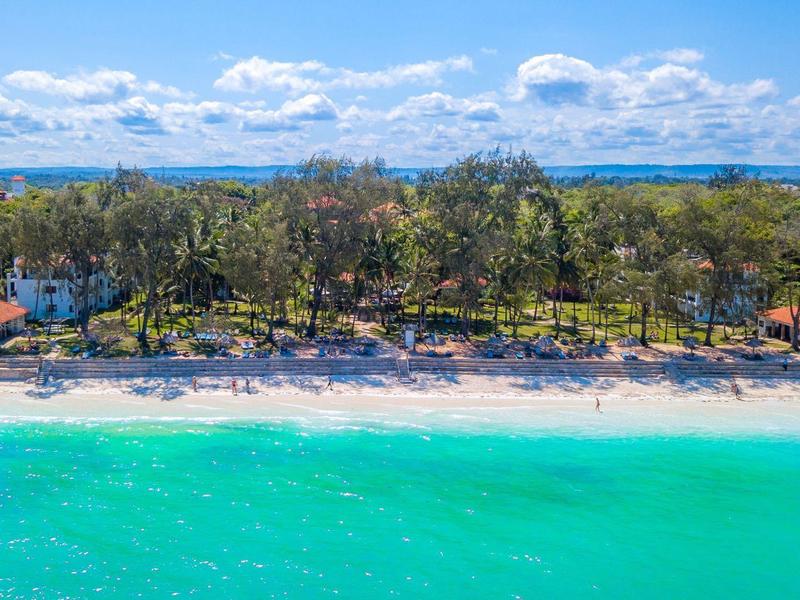 Strand met turquoise water, zand en beboste kustlijn met huizen op de achtergrond
