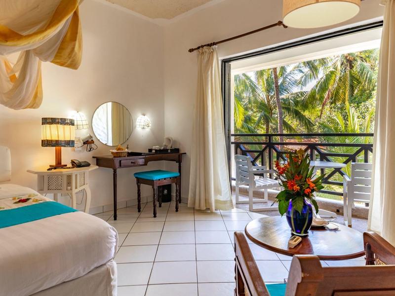 Licht ingericht hotelkamer met balkon met uitzicht op tropische palmbomen.