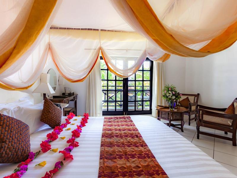 Lichte hotelkamer met schuine plafond, groot bed, bloemen en zithoek met stoelen en tafel