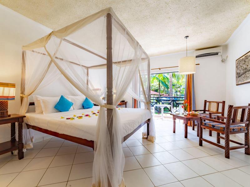 Lichte hotelkamer met hemelbed, blauwe sierkussens en uitzicht op het zwembad.