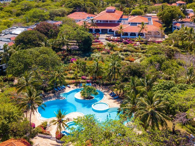 Luchtfoto van een resort met groot zwembad omringd door bomen en gebouwen