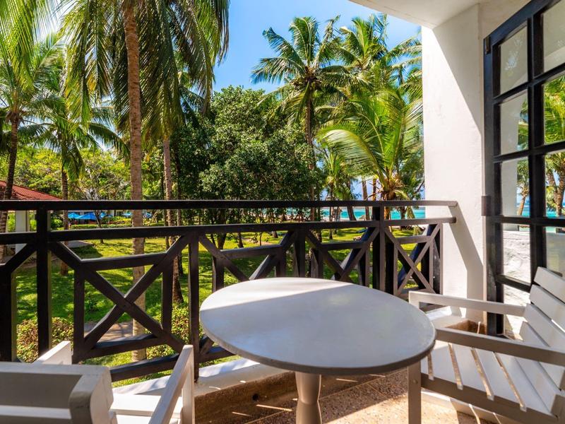 Balkon met ronde tafel en stoelen met uitzicht op tropische palmbomen en blauwe lucht.